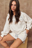 Woman wearing a white sweatshirt and shorts with blue accents against a brown background