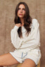 Woman wearing a white loungewear set with blue piping against a brown background