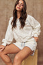 Woman wearing a white sweatshirt and shorts with blue stripes against a brown background