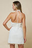 Woman wearing a white dress with thin straps and fringe details on a beige background