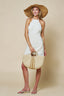 Woman in a white dress and straw hat holding a straw bag against a beige background