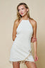 Woman wearing a white halter neck dress with gold fringe details on a beige background