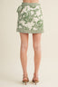 Green and white patterned skirt worn by a person on a beige background