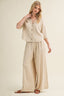 Woman wearing a beige outfit with wide-leg pants on a plain background