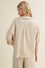Woman wearing a beige linen shirt and pants on a plain background