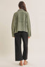 Person wearing a green jacket and black pants on a beige background