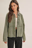 Woman wearing a green denim jacket over a white top and black pants on a beige background