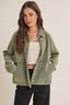 Woman wearing a green denim jacket over a white top and black pants on a beige background