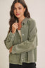Woman wearing a green denim jacket with a checkered collar on a plain background