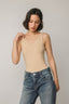 Woman wearing a beige tank top and blue jeans against a plain background