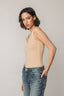 Woman wearing a beige tank top and blue jeans against a plain background