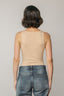 Person wearing a beige tank top and blue jeans against a plain background