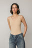 Woman wearing a beige tank top and blue jeans against a plain background