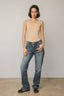 Woman wearing a beige tank top and blue jeans against a plain background