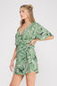 Woman wearing a green leaf-patterned romper on a white background