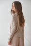 Woman wearing a beige long-sleeve top and pants against a white background