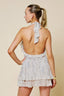Woman wearing a light-colored dress with a halter neck and ruffled layers on a beige background