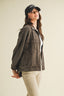 Woman wearing a dark denim jacket and cap on a plain background