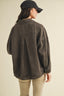 Person wearing a brown jacket and black cap on a beige background