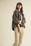 Person wearing a dark jacket and beige pants on a plain background