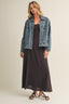 Woman wearing a denim jacket over a black dress on a beige background