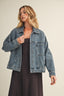 Woman wearing a denim jacket over a black dress on a beige background