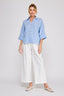 Woman wearing a light blue striped shirt and white pants on a white background