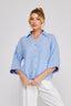 Woman wearing a light blue checkered blouse with white pants on a plain background