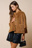 Woman wearing a brown teddy coat with black leather shorts and handbag on a beige background