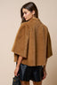 Woman wearing a brown poncho against a beige background