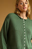 Woman wearing a green knitted cardigan with white buttons against a beige background