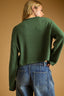 Person wearing a green sweater and blue jeans against a beige background