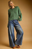 Woman wearing a green sweater and blue jeans against a beige background