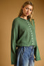 Woman wearing a green sweater with white buttons against a brown background