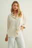 Woman wearing a beige shirt and white pants against a plain background