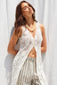 Woman wearing a white crochet cover-up over a striped swimsuit against a white curtain background
