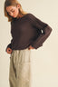 Slightly angled front view of the Driftwood Bateau Neck Crop Sweater in dark chocolate brown, showcasing the pronounced dropped shoulder, wide bateau neckline, and relaxed boxy fit with horizontal ribbed garter stitch knit