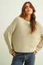 Woman wearing a beige knitted sweater and blue jeans against a plain background