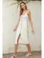 Woman wearing a white dress with buttons standing against a light-colored wall.