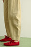 Beige pants and red shoes on a light green floor.