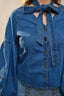 Woman wearing a blue denim blouse and neck accessory with a beige background