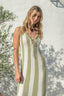 Woman wearing a green and white striped dress against a white wall with greenery.