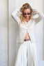 Woman wearing a white cardigan and pants with sunglasses indoors.