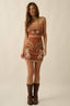 Woman wearing a patterned dress with cowboy boots on a beige background