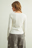 Woman wearing a white ribbed sweater and gray pants with bow patterns on a plain background