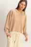 Woman wearing a beige sweatshirt and pants against a plain background