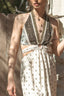 A woman wearing a bohemian-style two-piece halter dress set with a dark brown and beige paisley print on the top and a cream-colored skirt with a small geometric pattern.