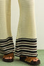 Person wearing a beige crochet skirt with black stripes and brown sandals on a plain background
