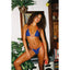 Woman in a blue and red bikini standing indoors with plants and a bookshelf in the background.