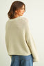 Woman wearing a beige knitted sweater and blue jeans on a plain background